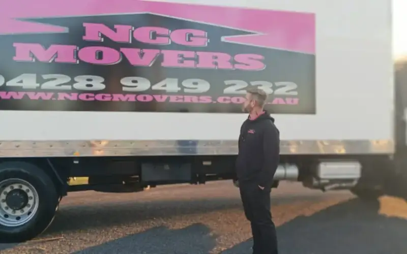 An NCG Movers crew member standing beside the truck in low afternoon sun