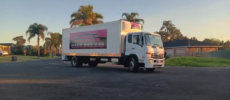 An NCG Movers truck on a palm-lined suburban street in low afternoon sun